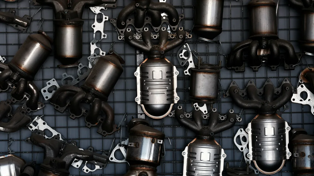 A collection of metal parts, including exhaust components, arranged on a grid-patterned surface.