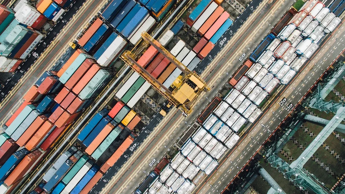 A large number of shipping containers, stacked horizontally and vertically, with some on train tracks and others on the ground, in a port or