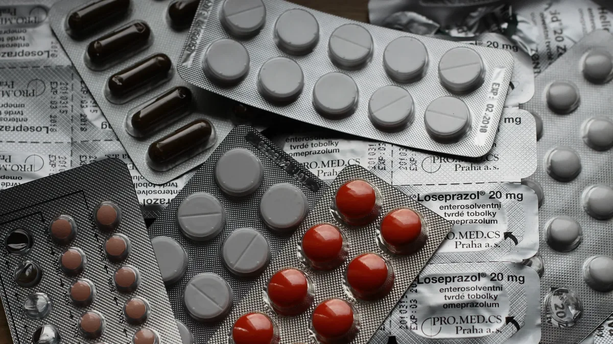 A collection of various pills and medication packaging, including blister packs and capsules, arranged on a surface.