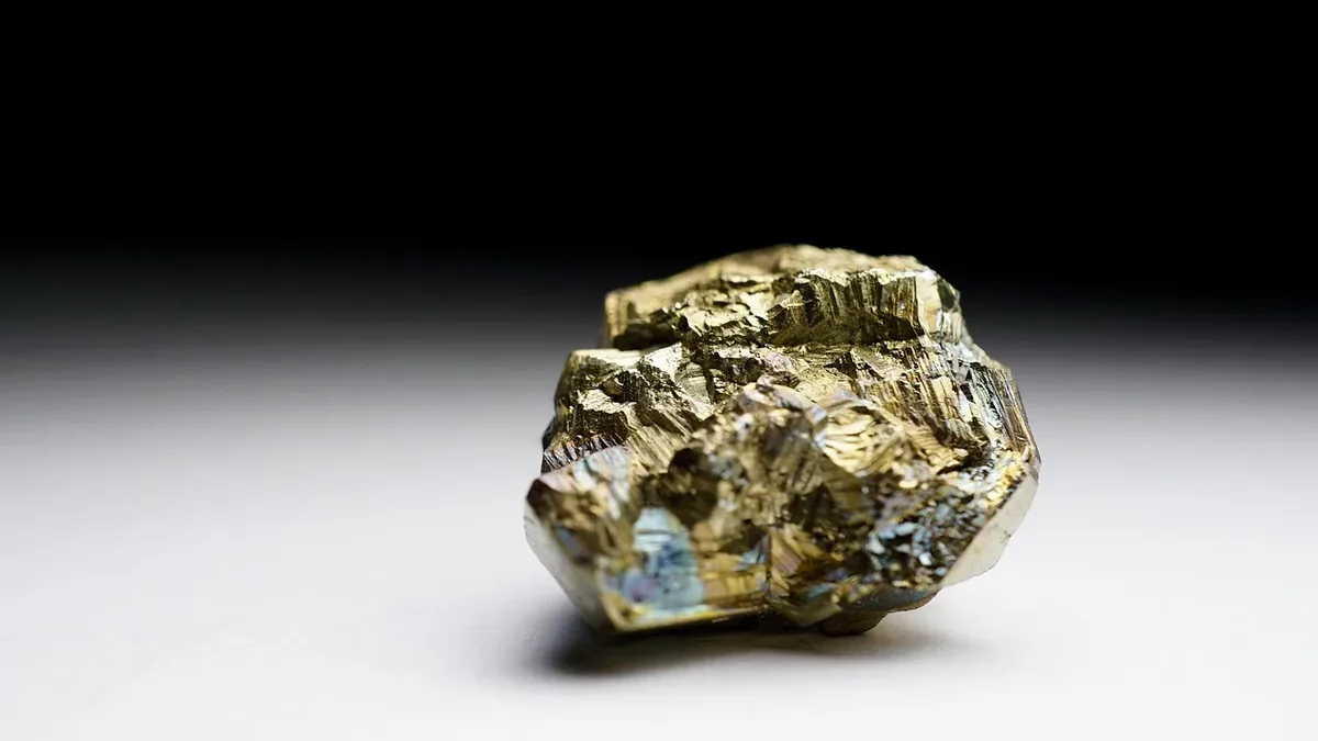 A rough, gold-colored mineral or rock with visible crystalline structures and a metallic sheen.