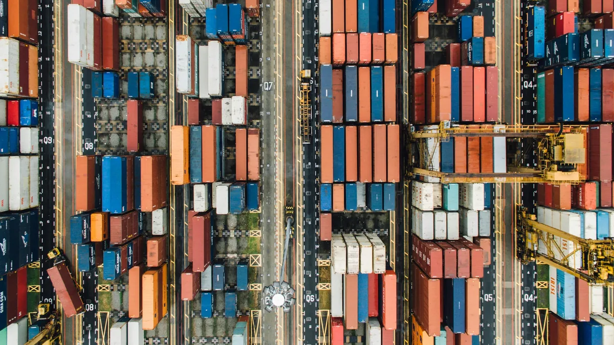 A large number of shipping containers stacked on top of each other in a port or warehouse, with a road running through the center.