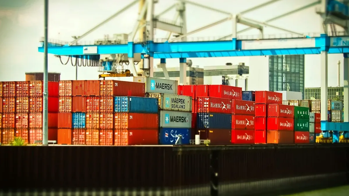 A large cargo ship carrying numerous shipping containers, with a crane visible in the background.