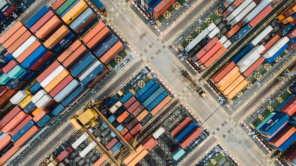 A large number of shipping containers stacked in rows, with some containers on the ground and others on top of each other, in a shipping yar