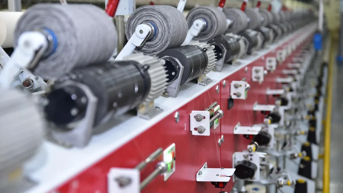 A long, red and white machine with multiple spools of thread or yarn on it, likely used for textile manufacturing.